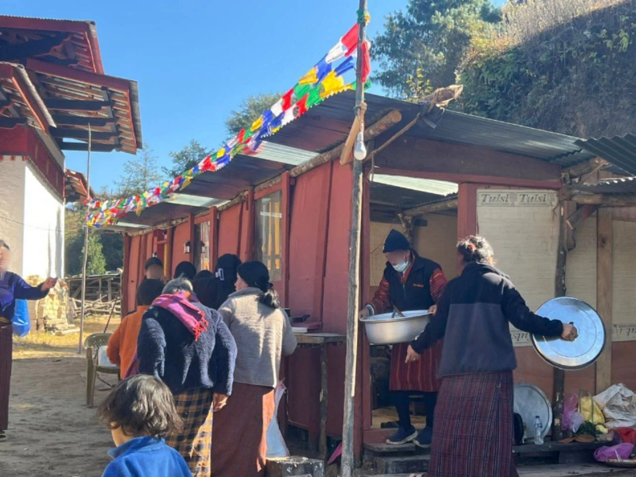 大众在悬挂经幡的红色建筑外，围着大盆分餐。