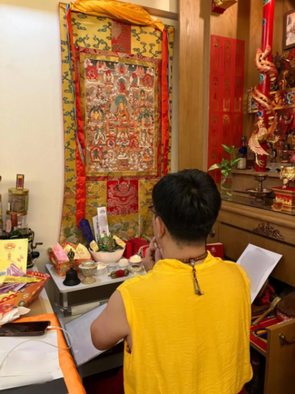 身着黄色法衣的修持者面向宗教挂画与摆放供品的坛场。